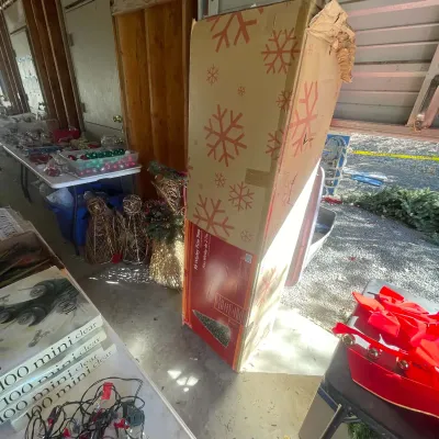 Sale Photo Thumbnail #121: A 9-foot Wesley Pine artificial Christmas tree in its original box, surrounded by various holiday decorations and string lights.