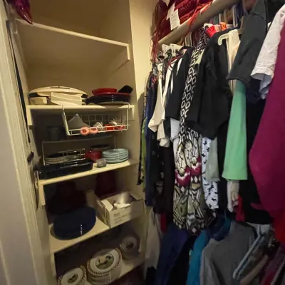 Sale Photo Thumbnail #74: Walk-in closet filled with assorted women's clothing on hangers alongside shelves stocked with kitchenware, dishes, and small appliances.
