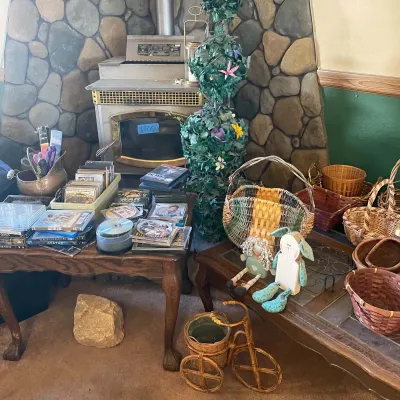 Sale Photo Thumbnail #59: Collection of home decor items including woven baskets, artificial greenery topiary, CDs, DVDs, and a small decorative wicker tricycle plant stand.