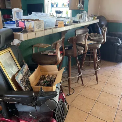 Sale Photo Thumbnail #55: Set of mid-century swivel barstools with brown vinyl seats alongside a mobility chair holding a cardboard box filled with vintage flatware.