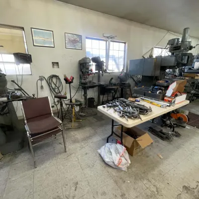 Sale Photo Thumbnail #102: Workshop equipped with heavy industrial machinery, including drill presses and milling equipment, alongside hand tools and a folding work table.