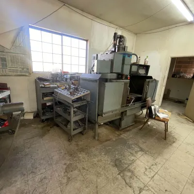 Sale Photo Thumbnail #99: Large vintage industrial CNC milling machine set up in a workshop alongside tool storage carts and accessories.