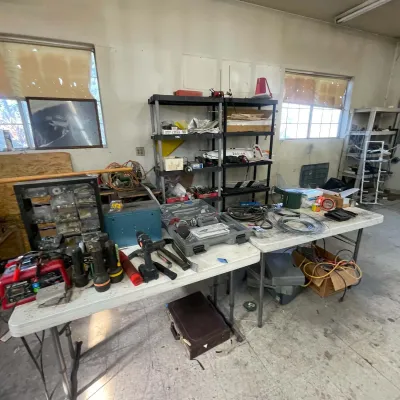 Sale Photo Thumbnail #97: Assorted workshop tools, power equipment, hardware organizers, and supplies arranged on folding tables and black plastic shelving units.