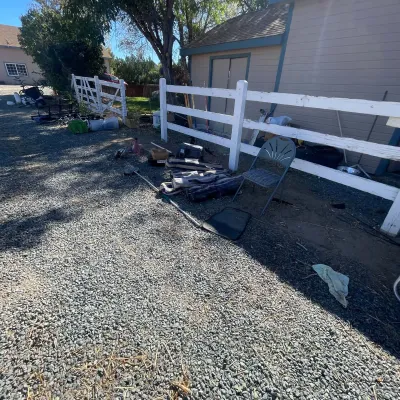 Sale Photo Thumbnail #37: Outdoor yard sale area featuring a metal folding chair, long-handled pool skimmer, camp chairs in bags, and various tools along a white wooden fence.
