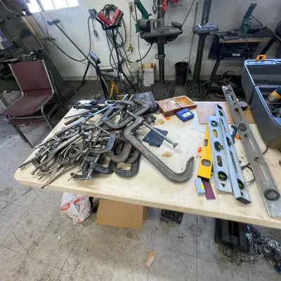 Sale Photo Thumbnail #105: Large assortment of metal workshop tools including C-clamps, locking pliers, and spirit levels displayed on a folding table.