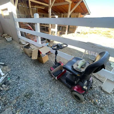 Sale Photo Thumbnail #110: Red Pride Go-Go four-wheel mobility scooter parked outdoors near cardboard storage boxes.