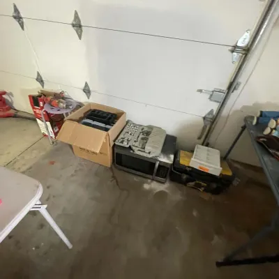Sale Photo Thumbnail #33: Assorted workshop items and electronics, including a socket set, microwave, toolboxes, power tools, and storage containers set against a garage wall.