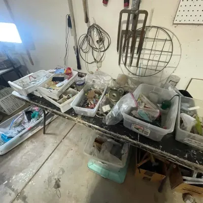 Sale Photo Thumbnail #31: Workshop folding tables loaded with clear plastic storage bins containing assorted crafting supplies, hardware, and miscellaneous small items, alongside wall-mounted garden tools.