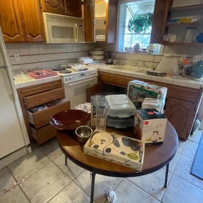 Sale Photo Thumbnail #119: Round wooden kitchen table display featuring boxed housewares, a dog feeding set, a large ceramic bowl, glassware, and small kitchen items.