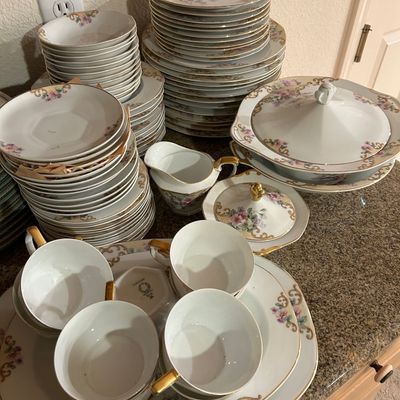 Sale Photo Thumbnail #41: Large vintage porcelain dinnerware service featuring delicate floral motifs, gold trim detailing, stacked plates, teacups, serving platters, and a covered tureen.