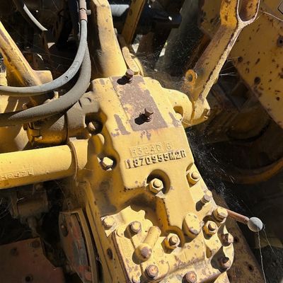 Sale Photo Thumbnail #120: Vintage yellow tractor hydraulic housing assembly showing serial number 1870955M2R, featuring cobwebs and surface rust from age and use.