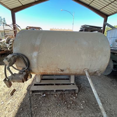 Sale Photo Thumbnail #125: Large steel fuel transfer tank with mounted electric pump, resting on a wooden pallet in an open-air shed.