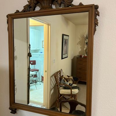 Sale Photo Thumbnail #17: Vintage wood-framed wall mirror featuring an ornate carved floral pediment crest and detailed bottom corner accents.