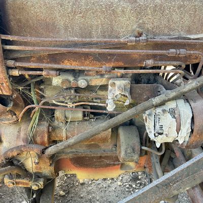 Sale Photo Thumbnail #119: Vintage tractor or heavy machinery engine block showing extensive rust, cobwebs, and aged fuel or hydraulic lines.