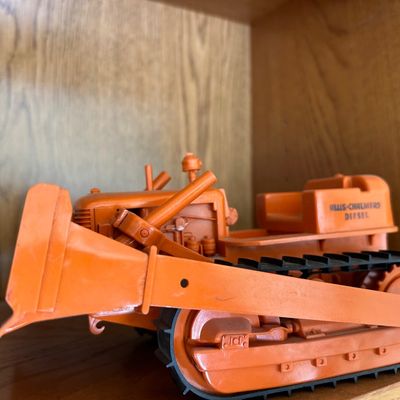 Sale Photo Thumbnail #115: Vintage Allis-Chalmers Diesel toy crawler tractor featuring a front dozer blade and rubber treads, displayed on a wooden shelf.