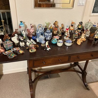 Sale Photo Thumbnail #84: Vintage mahogany sofa table with drop leaves and two drawers, topped with a large collection of porcelain figurines, ceramics, teapot sets, and decorative collectibles.