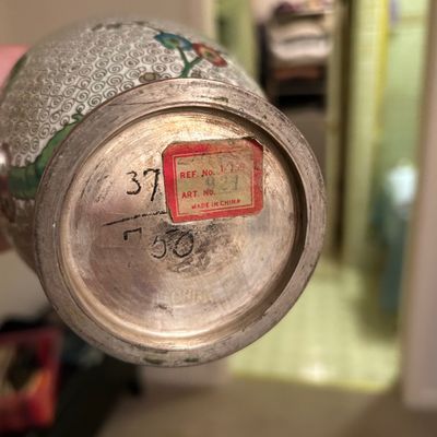 Sale Photo Thumbnail #72: Underside of a vintage Chinese cloisonné vase showing a metal base with an import label marked 'Made in China' and hand-written numbers.