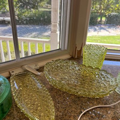 Sale Photo Thumbnail #26: Collection of yellow Vaseline glass dishes featuring a daisy and button pattern, displayed near a window.