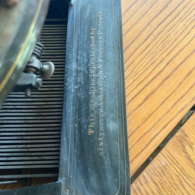 Sale Photo Thumbnail #110: Detail view of an antique Oliver typewriter showing patent lettering on the metal base, featuring gold pinstriping and original painted text.