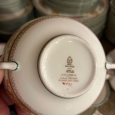 Sale Photo Thumbnail #40: Underside of a Wedgwood Columbia (W595) porcelain vessel showing the maker's mark and 1925 patent date, displayed with matching dinnerware.