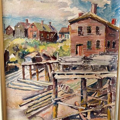 Sale Photo Thumbnail #145: Framed watercolor painting depicting a coastal village scene with buildings and wooden docks, set in a simple metallic frame.