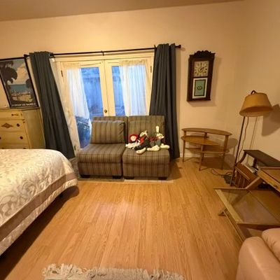 Sale Photo Thumbnail #192: Bedroom featuring a pair of striped armless chairs, a mid-century style tiered side table, a tall dresser, and wall clock.