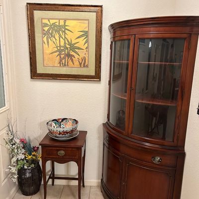 Sale Photo Thumbnail #85: Traditional mahogany rounded corner hutch with glass doors alongside a small side table and framed Asian-style bamboo art.