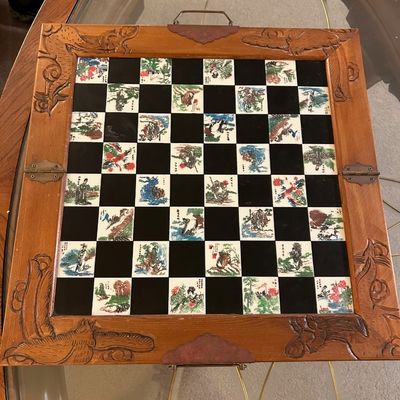 Sale Photo Thumbnail #77: Vintage Asian-style carved wood chessboard featuring inlaid porcelain tiles with detailed hand-painted scenes and brass hardware.
