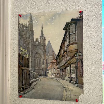 Sale Photo Thumbnail #153: Unframed watercolor painting depicting a European street scene with a cathedral, pinned directly to a wall.