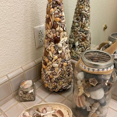 Sale Photo Thumbnail #65: Collection of coastal-themed decor featuring a tall sea shell cone tree, a glass jar filled with shells and beach finds, and a shallow ceramic dish with assorted shells.