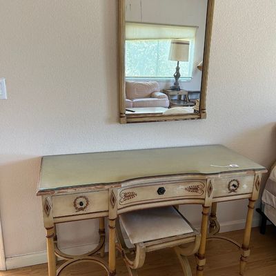 Sale Photo Thumbnail #180: French Neoclassical-style vanity desk set featuring a distressed off-white painted finish, glass top, matching vanity stool, and a tall carved wall mirror.
