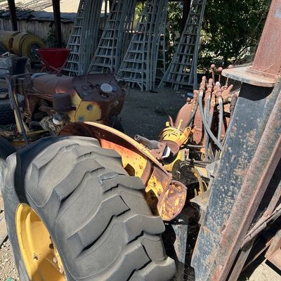 Sale Photo Thumbnail #129: Vintage yellow farm tractor with large rear tire and visible hydraulic lines, shown in an open shed alongside several tall extension ladders.