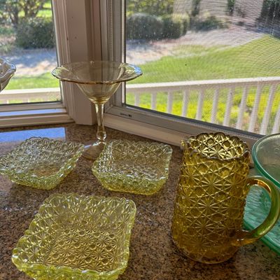 Sale Photo Thumbnail #23: Collection of yellow and amber Depression glass pieces, including a small pitcher, three daisy and button pattern dishes, and a tall stemmed glass.
