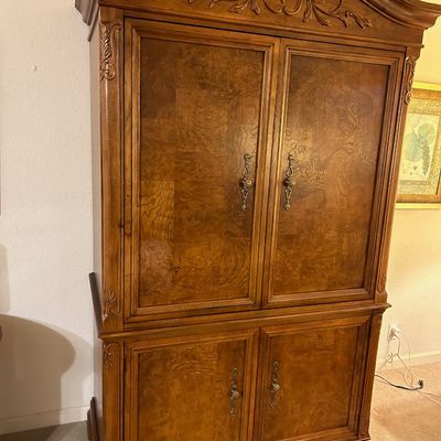Sale Photo Thumbnail #87: Traditional wooden armoire featuring burl wood door panels, floral wood carvings along the crown moulding, and ornate brass hardware.