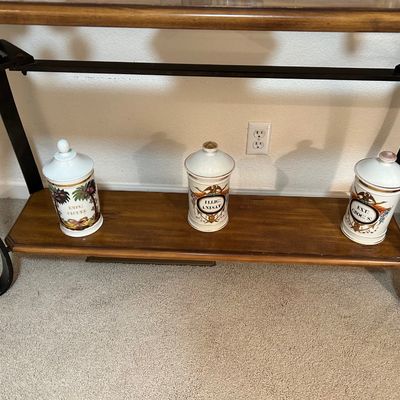 Sale Photo Thumbnail #59: Set of three vintage ceramic apothecary jars displayed on the lower shelf of a wooden console table with a black metal frame.