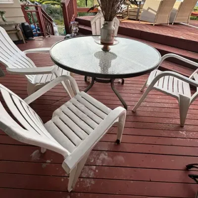 Sale Photo Thumbnail #14: Outdoor patio set featuring a round glass-top table with metal frame surrounded by white plastic resin armchairs on a wooden deck.