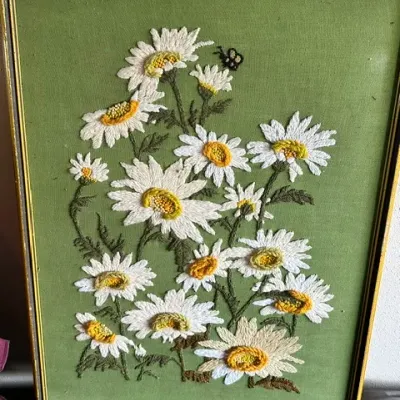Sale Photo Thumbnail #33: Framed vintage crewel embroidery piece featuring white daisies and a small bee on a green fabric background.