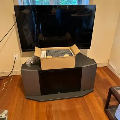 Sale Photo Thumbnail #16: Flat-screen TV mounted above a black corner media cabinet, with an open box containing electronics resting on the top shelf.
