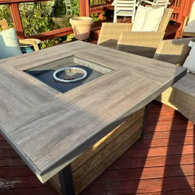 Sale Photo Thumbnail #11: Square outdoor propane fire pit table with faux-wood tile top, set alongside matching wicker patio chairs.