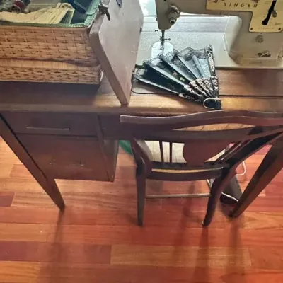 Sale Photo Thumbnail #34: Vintage Singer sewing machine set into a wooden sewing desk with matching chair, accompanied by a woven sewing basket and a decorative hand fan.