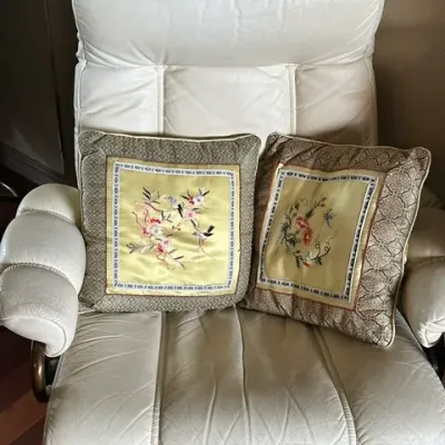 Sale Photo Thumbnail #35: Off-white leather or vinyl swivel recliner with high back and segmented cushioning, paired with two Asian-style silk embroidered throw pillows.