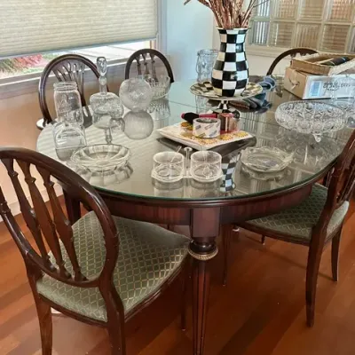 Sale Photo Thumbnail #25: Traditional oval wooden dining table with a glass top, paired with shield-back chairs featuring upholstered green patterned seats, displayed with an assortment of glassware and decorative pieces.