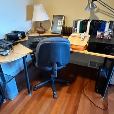 Sale Photo Thumbnail #15: L-shaped wooden office desk setup featuring a blue fabric rolling office chair, desk lamps, an Epson printer, binders, and assorted computer accessories.