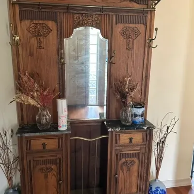 Sale Photo Thumbnail #32: Vintage carved oak hall tree featuring a central mirror, brass hooks, hat rack, and marble-top side cabinets.