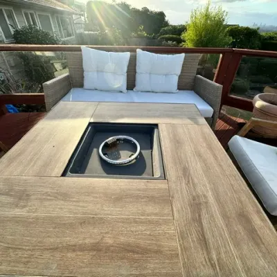 Sale Photo Thumbnail #12: Outdoor patio furniture set featuring a wood-look square propane fire pit table surrounded by a woven loveseat and armchairs with white cushions.