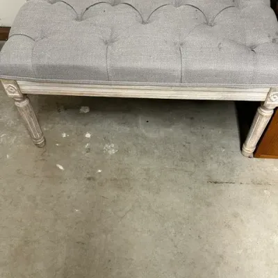Sale Photo Thumbnail #3: French provincial-style upholstered bench with a button-tufted grey cushion and whitewashed turned legs, showing minor wear on the fabric.