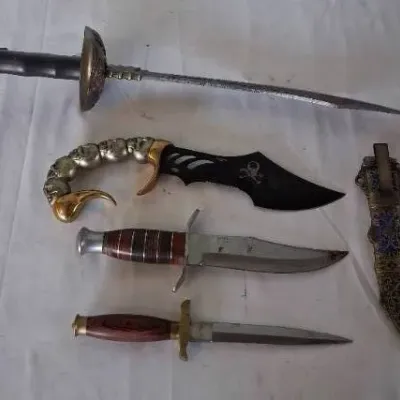 Collection of decorative and vintage blades, including a rapier-style sword, a skull-motif fantasy knife, fixed-blade hunting knives, and...