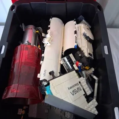 Large black plastic storage bin filled with partially assembled Lego NASA Space Shuttle Discovery set pieces.