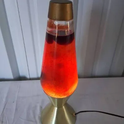 Vintage Lava Lite brand lava lamp featuring a gold-toned metal base and top cap with red fluid and dark wax.