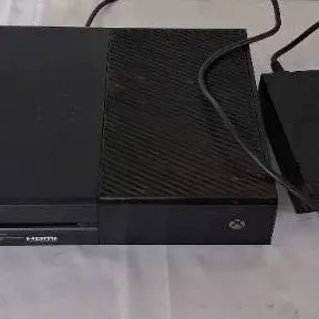 Original Microsoft Xbox One video game console in matte black with accompanying power supply brick.